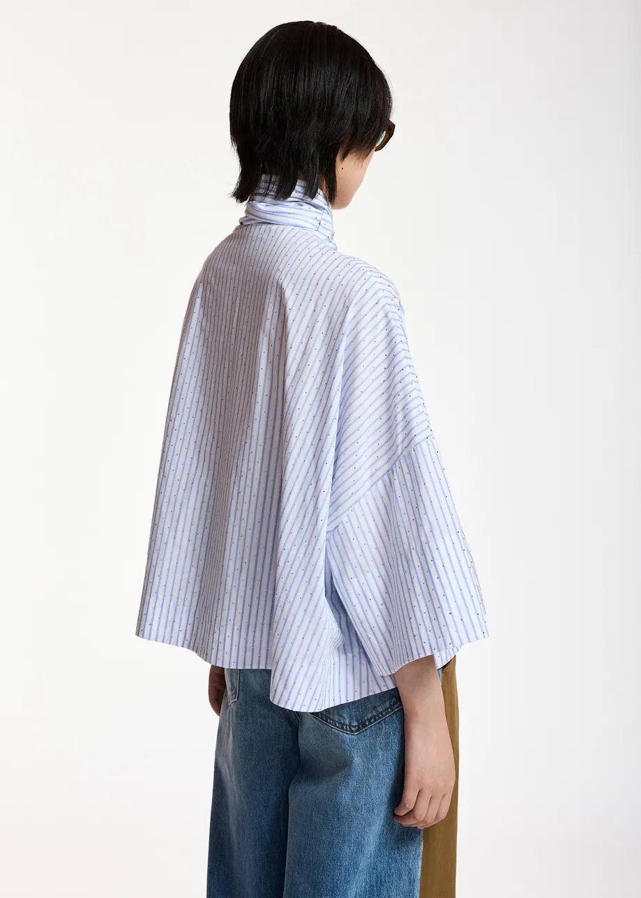 A model shown from the back wearing a light blue and white vertically striped high-neck shirt with wide three-quarter sleeves, paired with blue jeans, against a plain white background.