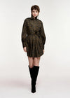A model wearing a dark olive green and black leopard-print mini dress with a high collar and long sleeves, paired with black over-the-knee boots, shot against a plain light gray studio background.
