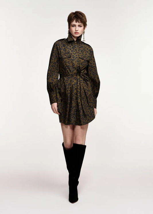 A model wearing a dark olive green and black leopard-print mini dress with a high collar and long sleeves, paired with black over-the-knee boots, shot against a plain light gray studio background.