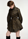 A model wearing a dark olive green and black leopard print mini dress with a tie waist belt, styled with black knee-high socks against a plain white studio background.