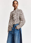 A model wearing a long-sleeve leopard print blouse with a ruffled high collar, paired with blue jeans, against a plain light gray background.