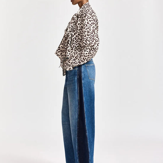 A model shown in profile wearing a leopard-print long-sleeve shirt, wide-leg blue jeans with dark side panels, and burgundy pointed-toe heeled boots, against a plain light gray studio background.