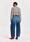 A model shown from the back wearing a leopard-print long-sleeve shirt, blue wide-leg jeans with dark side panels, and brown pointed-toe boots, against a plain light gray studio background.