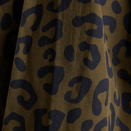 Close-up of a leopard print fabric with dark navy blue spots on a warm brown background.