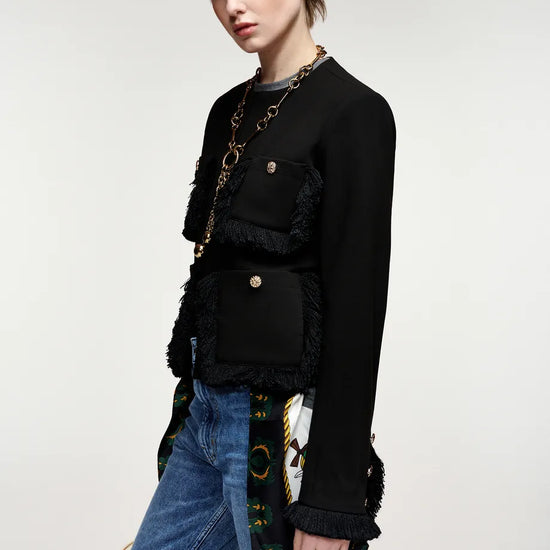 A model wearing a black fringed jacket with gold-tone hardware, layered over a gray top and paired with blue jeans, photographed against a plain light gray studio background.
