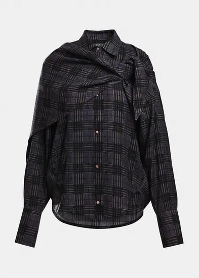 A black and gray plaid button-down shirt with an asymmetrical draped collar and long sleeves, shown against a light gray background.
