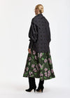 A model is shown from the back wearing a dark gray and black plaid shawl collar jacket over a dark green midi skirt with a pink floral pattern, paired with black ankle boots.