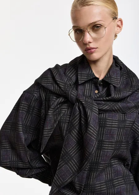 A close-up of a model wearing a dark plaid button-up shirt with voluminous sleeves and a matching scarf draped around the shoulders, set against a plain white background.