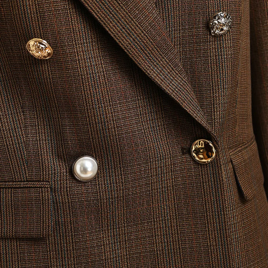 Close-up of a brown plaid double-breasted blazer with decorative buttons, including a pearl button and textured gold and silver buttons.
