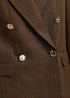 Close-up of a brown plaid double-breasted blazer with decorative buttons, including a pearl button and textured gold and silver buttons.