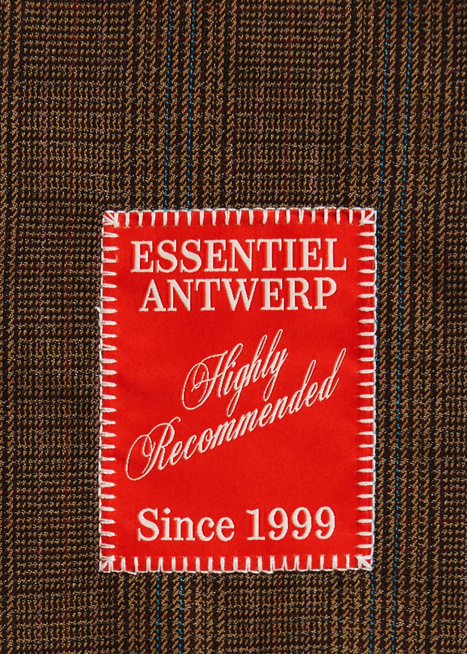 A close-up of a brown and black plaid fabric with a prominent red rectangular patch reading 'ESSENTIEL ANTWERP Highly Recommended Since 1999' in white text.
