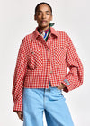 A model wearing a red and white checkered cropped jacket with front pockets, styled with a colorful neck scarf and light blue jeans against a plain light gray background.