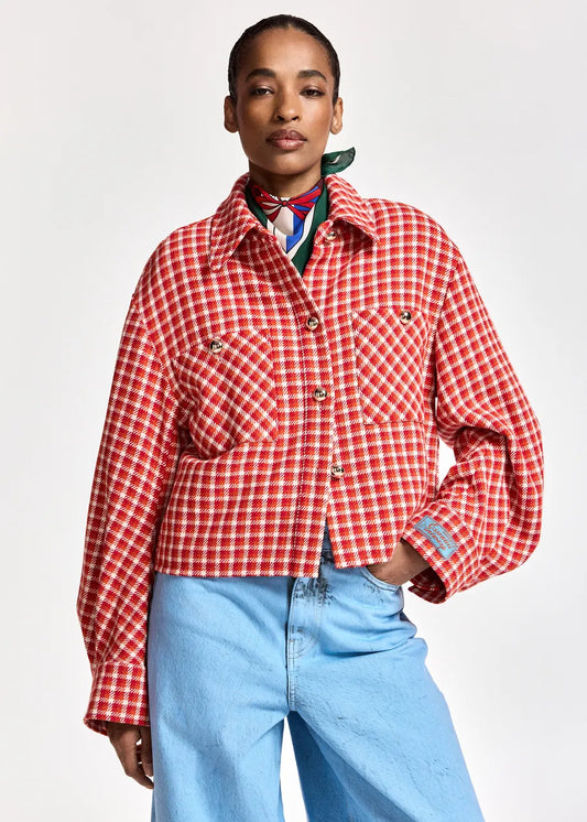 A model wearing a red and white checkered cropped jacket with front pockets, styled with a colorful neck scarf and light blue jeans against a plain light gray background.