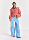 A model stands against a light gray studio background wearing a red and white gingham cropped button-up shirt, light blue wide-leg jeans, a multicolor striped necktie, and red shoes.