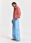 A model is shown from the side wearing a red and white gingham button-up shirt, light blue wide-leg denim jeans, and red shoes, set against a plain light gray studio background.