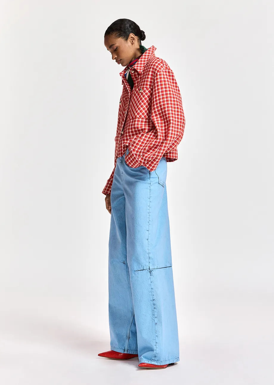 A model is shown from the side wearing a red and white gingham button-up shirt, light blue wide-leg denim jeans, and red shoes, set against a plain light gray studio background.