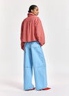 A model shown from the back wearing a red and white gingham check shirt, light blue wide-leg denim pants, and red pointed shoes, set against a plain light gray studio background.