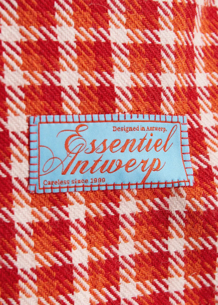 A close-up of a red, orange, and white plaid fabric with a central light blue sewn label reading 'Essentiel Antwerp'.