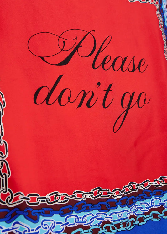 A close-up of a red fabric item, likely a scarf or bandana, featuring the phrase 'Please don't go' in black cursive script. The bottom edge is decorated with a multicolor chain-link pattern in shades of blue, white, and brown.