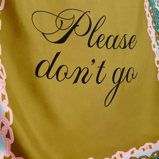 A close-up of a yellow-green fabric item, likely a scarf or sash, featuring the phrase 'Please don't go' in black cursive script. The fabric is finished with a decorative border in pink, green, and gold.