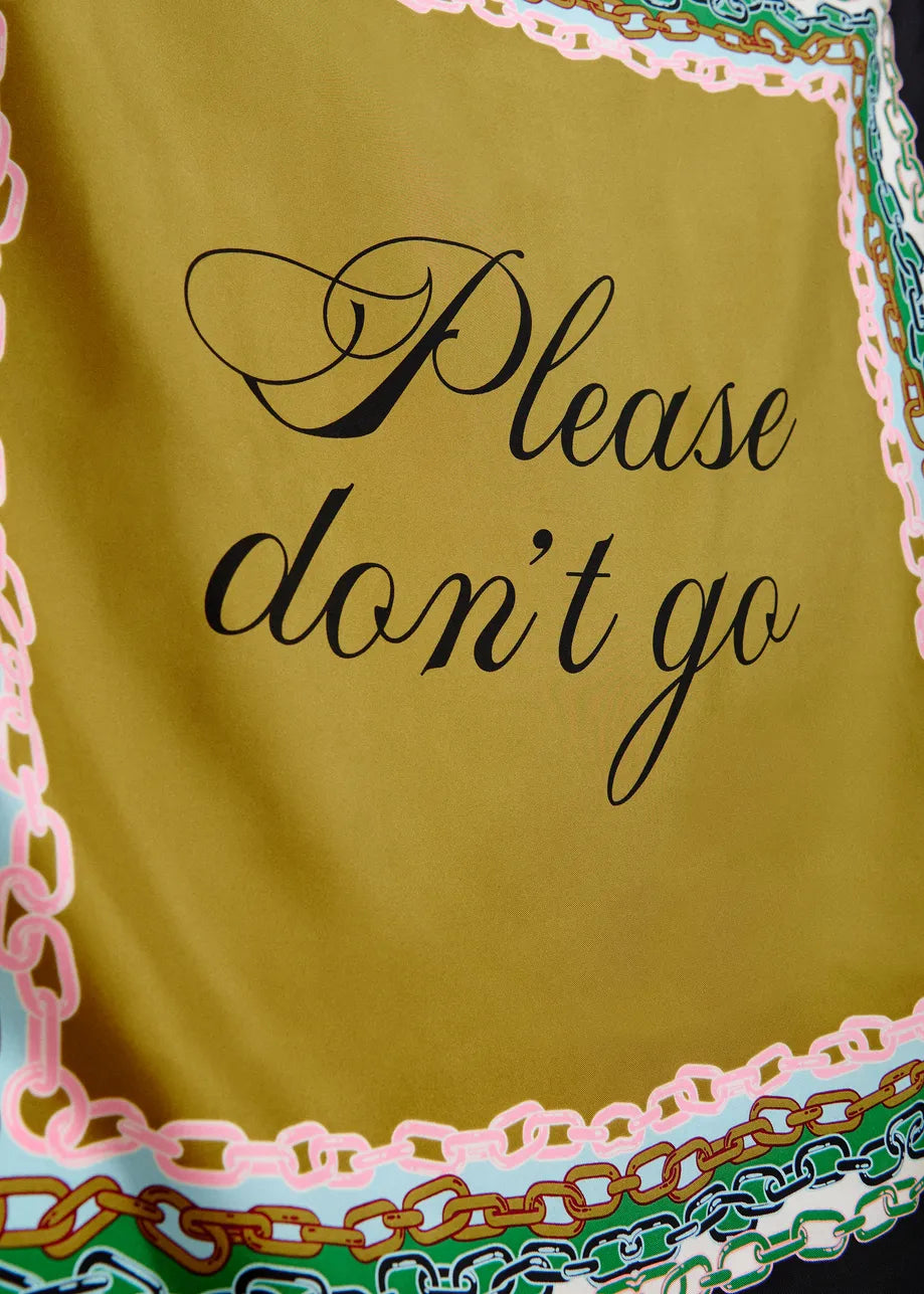 A close-up of a yellow-green fabric item, likely a scarf or sash, featuring the phrase 'Please don't go' in black cursive script. The fabric is finished with a decorative border in pink, green, and gold.