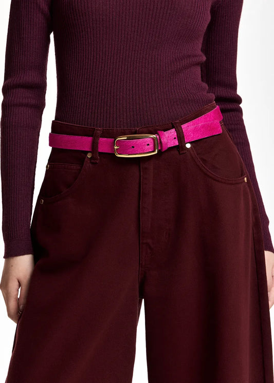 A close-up of a person wearing a bright pink belt with a gold-tone buckle over a burgundy ribbed long-sleeve top and matching wide-leg trousers.