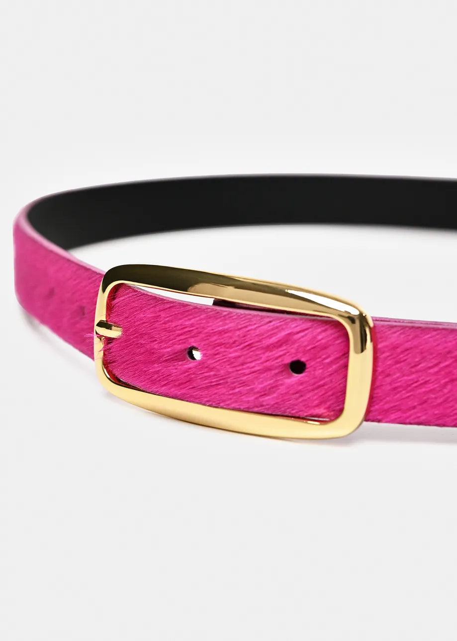 A close-up of a belt with a textured hot pink strap, a black interior lining, and a polished gold-tone metal buckle.