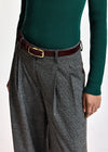 A close-up of a person wearing gray and black plaid wide-leg trousers with pleats, a dark brown leather belt with a gold buckle, and a dark green ribbed knit sweater.