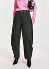 A model wearing dark olive green wide-leg denim jeans, styled with a pink sweater, black pointed-toe boots, and a black crossbody bag against a light gray studio background.