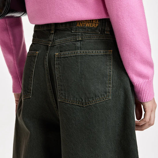 Close-up back view of a person wearing dark washed denim wide-leg jeans and a pink sweater, with the Antwerp brand patch visible on the jeans waistband.