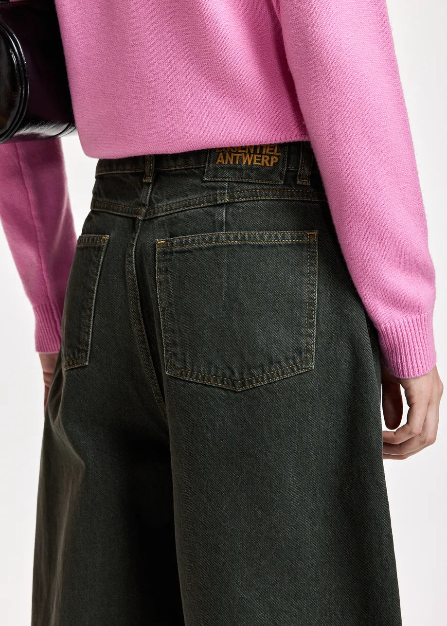 Close-up back view of a person wearing dark washed denim wide-leg jeans and a pink sweater, with the Antwerp brand patch visible on the jeans waistband.