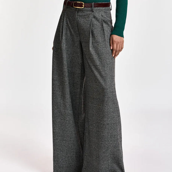 A model wearing high-waisted, wide-leg gray plaid trousers with a dark brown belt, paired with a dark green long-sleeve top and brown pointed-toe heels, against a plain white studio background.
