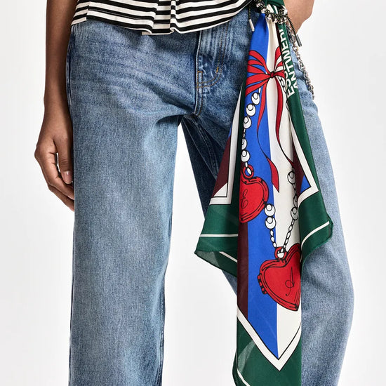 A close-up of a person wearing blue jeans and a black-and-white striped top, with a colorful patterned scarf tied around the waist over the jeans.