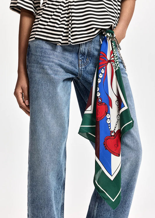 A close-up of a person wearing blue jeans and a black-and-white striped top, with a colorful patterned scarf tied around the waist over the jeans.