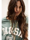Woman wearing a green t-shirt with 'BA&SH' branding and gold necklace.
