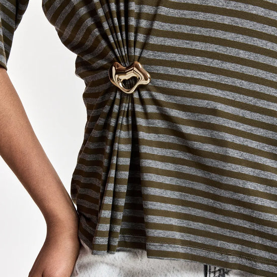 Close-up of a person wearing a horizontally striped knit top in olive green and heather gray, gathered at the waist with a metallic heart-shaped ring.