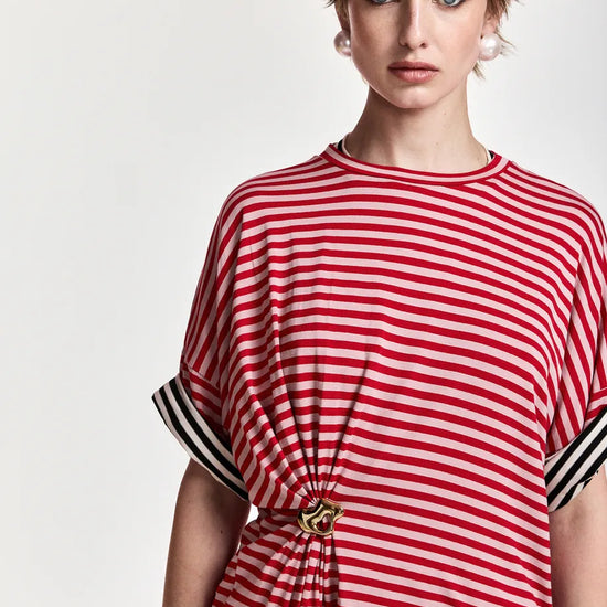 A model wearing a red and white horizontally striped short-sleeve top with black and white striped cuffs and a gold-tone decorative knot at the waist, set against a plain light background.