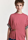 A model wearing a red and white horizontally striped short-sleeve top with black and white striped cuffs and a gold-tone decorative knot at the waist, set against a plain light background.
