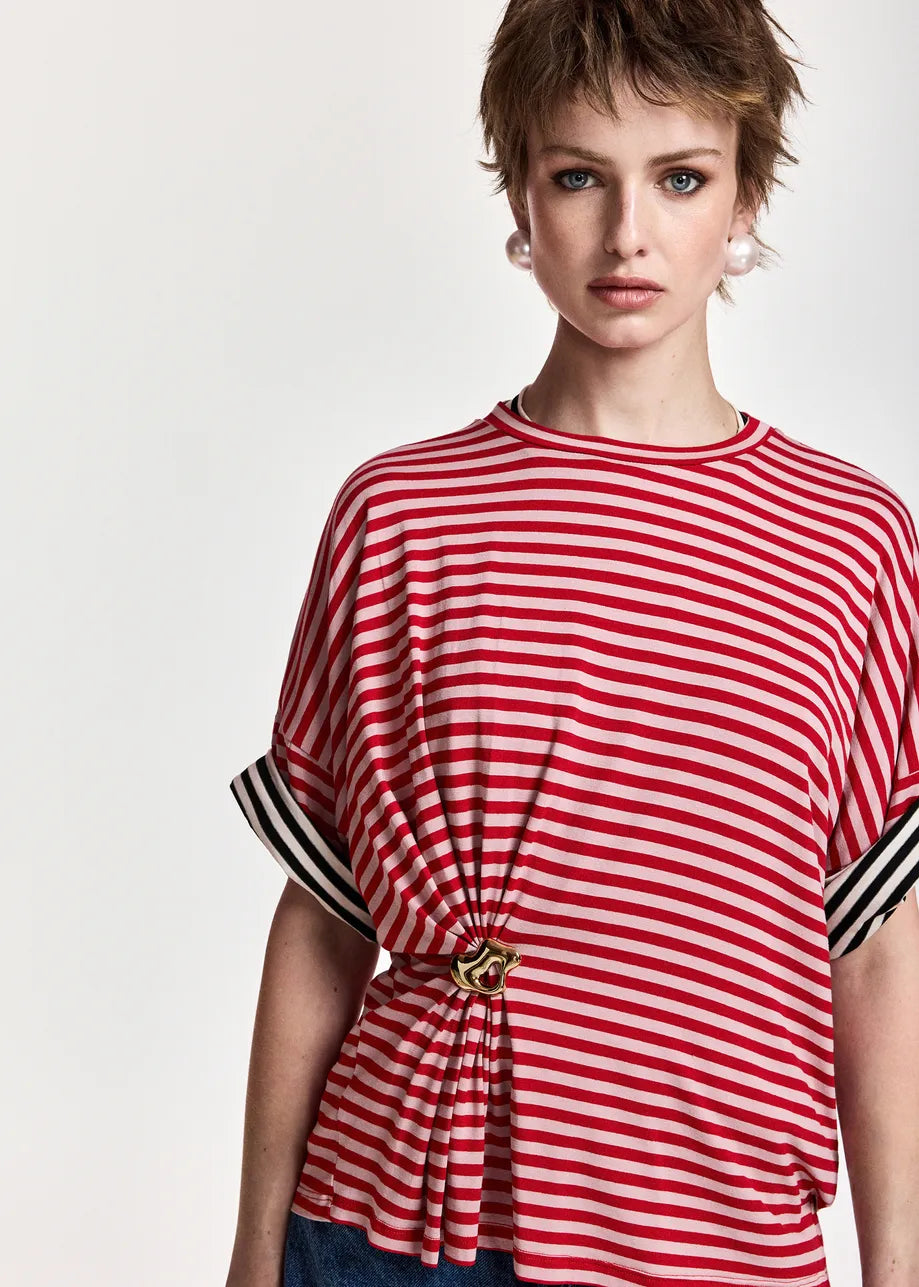 A model wearing a red and white horizontally striped short-sleeve top with black and white striped cuffs and a gold-tone decorative knot at the waist, set against a plain light background.