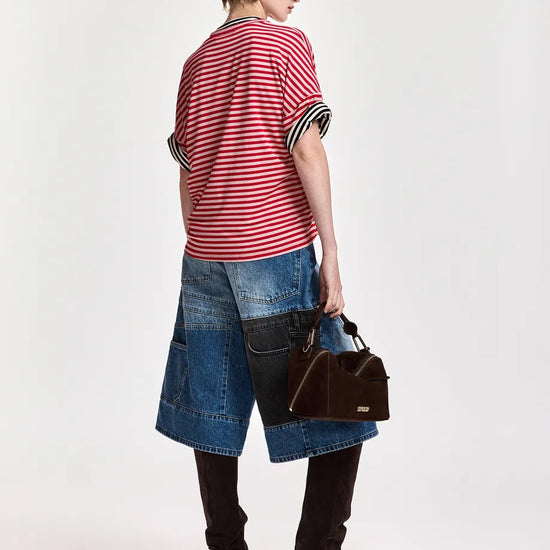A model shown from the back wearing a red and white striped short-sleeve top, a denim patchwork skirt, black over-the-knee boots, and holding a brown handbag against a plain white studio background.