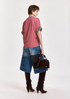 A model shown from the back wearing a red and white striped short-sleeve top, a denim patchwork skirt, black over-the-knee boots, and holding a brown handbag against a plain white studio background.