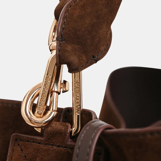 Close-up detail of a brown leather and suede handbag with gold-tone hardware and a visible brand engraving on the clasp.