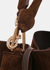Close-up detail of a brown leather and suede handbag with gold-tone hardware and a visible brand engraving on the clasp.