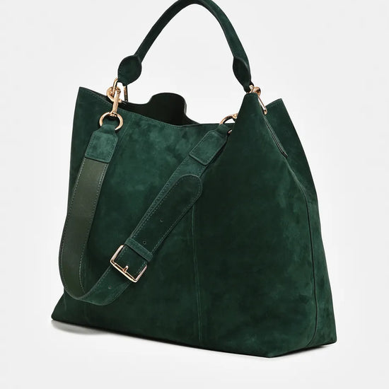 A dark green suede tote bag with a matching shoulder strap, gold-tone hardware, and top handles, shown on a light gray background.