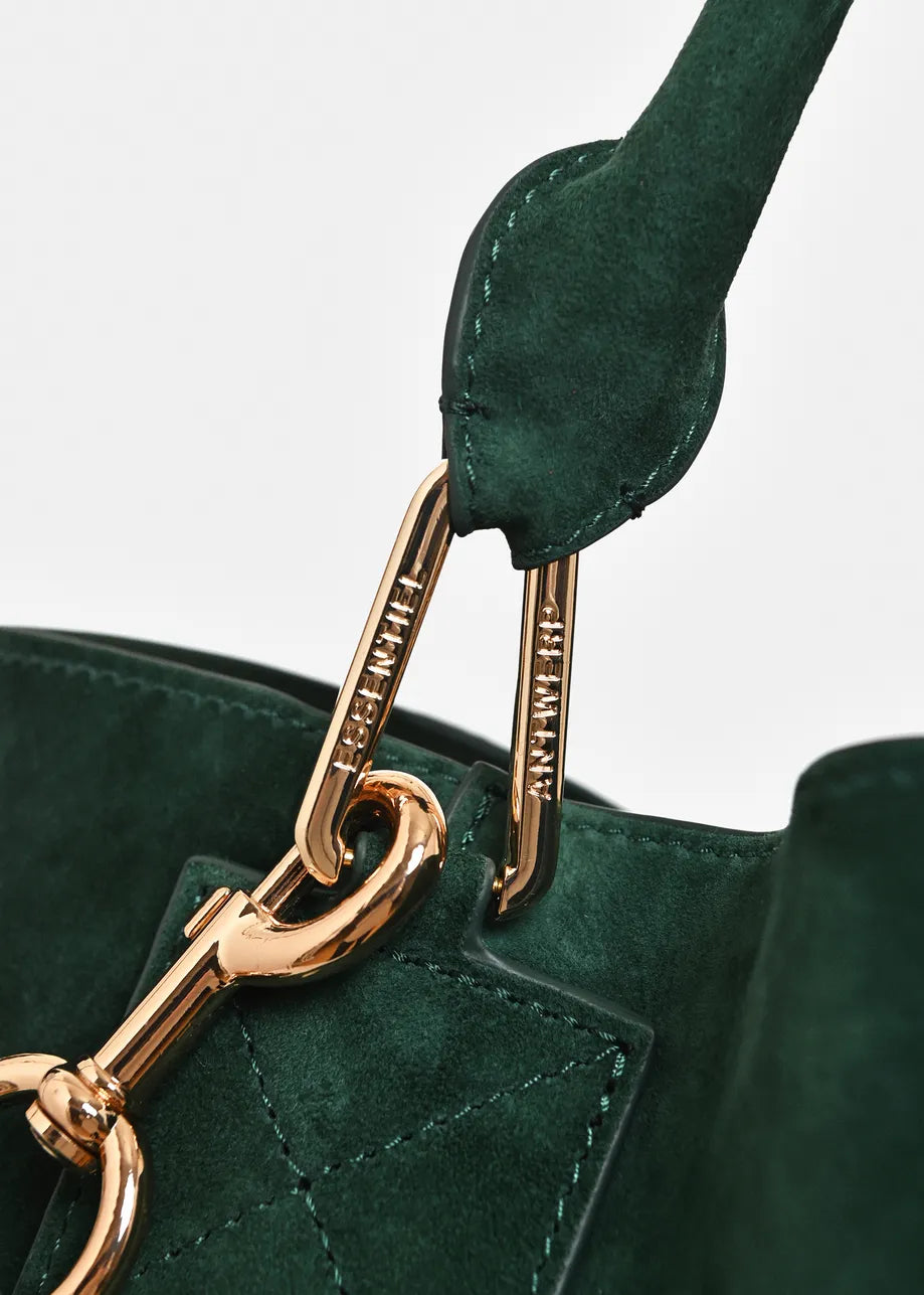 Close-up of a dark green suede handbag with gold-tone hardware and a matching green leather strap, showing engraved brand text on the clips.
