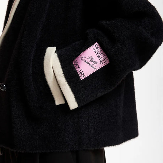 Close-up of a black fuzzy jacket with cream ribbed trim and a pink sleeve patch 