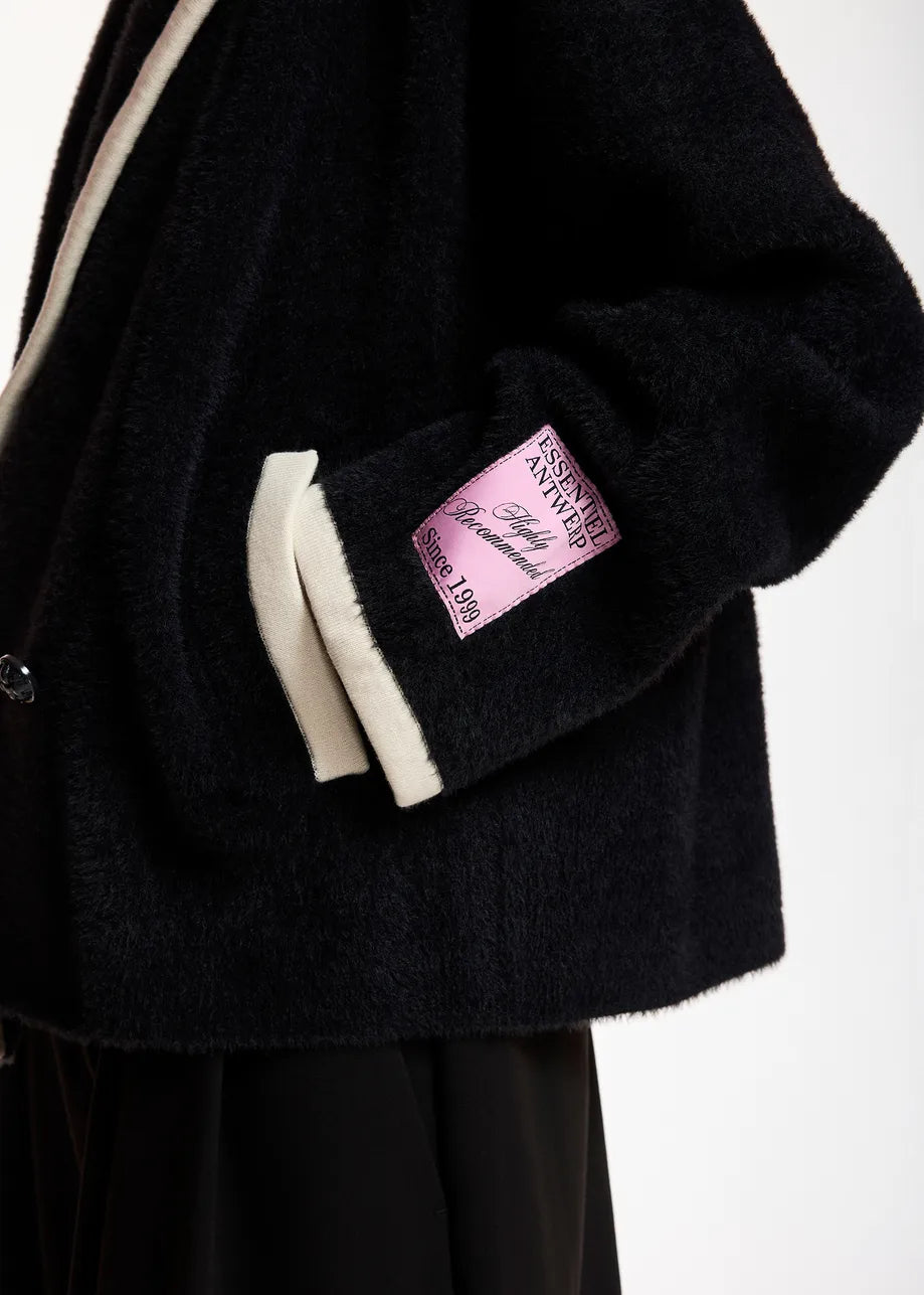 Close-up of a black fuzzy jacket with cream ribbed trim and a pink sleeve patch 
