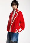 A model wearing a vibrant red fuzzy cropped jacket with cream-colored piping, paired with a white turtleneck and blue denim shorts, shot against a plain white studio background.