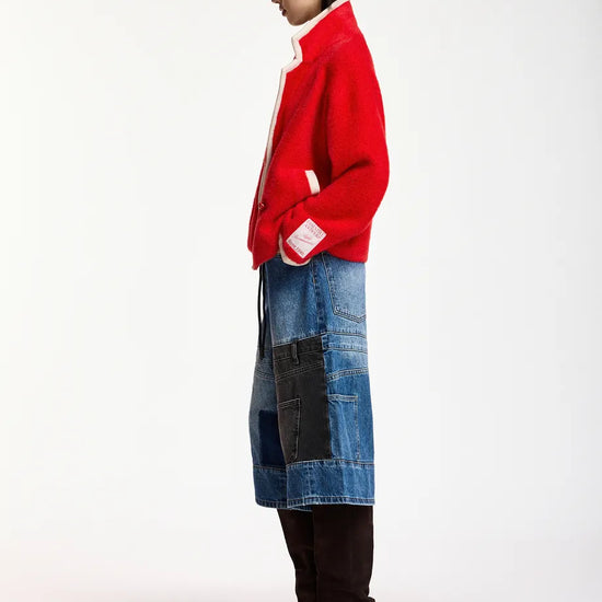 A model shown from the side profile wearing a bright red knit cardigan with white trim, a blue patchwork denim skirt, and dark brown knee-high heeled boots, set against a plain white studio background.