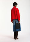 A model shown from the back wearing a bright red cropped cardigan, a blue denim patchwork skirt with a black pocket, and dark brown boots, against a plain white studio background.